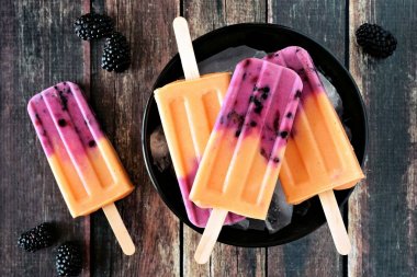 Kase mango blackberry yoğurt çubuklu dondurmayı, karanlık bir rustik ahşap arka plan üzerinde Üstten Görünüm