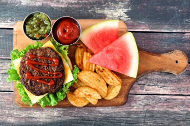 Piknik sahne açık hamburger, patates dilimleri ve rustik ahşap üzerinde bir kürek tahtada karpuz