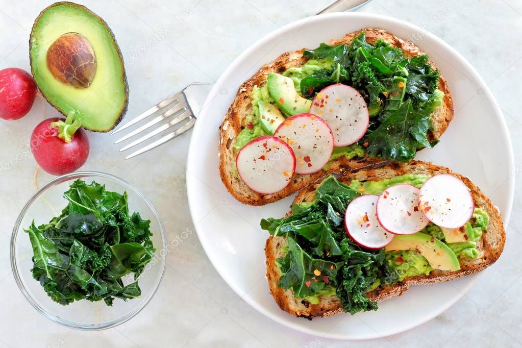 Avocado toast with kale and radish on whole grain bread, overhead scene on marble