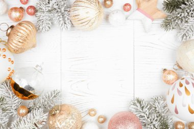 Karlı dallardan, tozlu güllerden, altınlardan ve beyaz süslemelerden oluşan bir Noel çerçevesi. Beyaz ahşap arka planda üst görünüm.