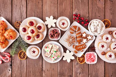 Karışık tatlı ve kurabiyelerin olduğu Noel masası sahnesi. Kırsal ahşap arka planda manzaranın üstünde. Tatil pişirme konsepti.