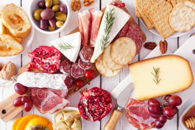 Şarküteri kurulu çeşitli peynirler, etler ve aperatifler. Beyaz ahşap bir arka planda en üstteki tablo sahnesi.