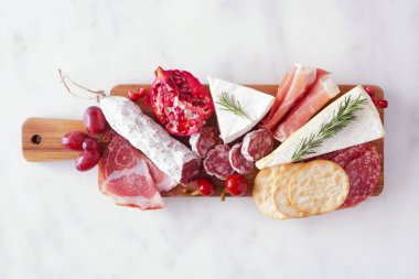 Etler, peynirler ve aperatifler servis ediliyor. Beyaz mermer arka planda üst görünüm.