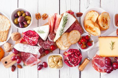 Şarküteri kurulu çeşitli peynirler, etler ve aperatifler. Masanın üstünde beyaz ahşap bir arka planda..