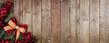 Christmas corner border banner with red and black checked buffalo plaid ribbon, burlap and tree branches. Top view on a rustic wood background.
