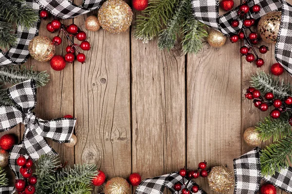 Christmas frame with white and black checked buffalo plaid ribbon, baubles and tree branches. Top view on a rustic wood background.