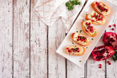 Brie peyniri, nar ve maydanozlu bayram crostini mezeleri. Masanın üstündeki beyaz ahşap arka planda fotokopi alanı var. Parti yemeği konsepti.