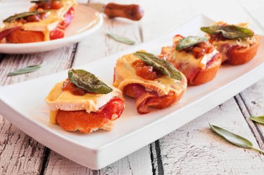 Parma jambonlu crostini aperatifleri, mavi peynir ve çıtır adaçayı. Beyaz ahşap arka planda servis tabağına yakın dur. Parti yemeği konsepti.