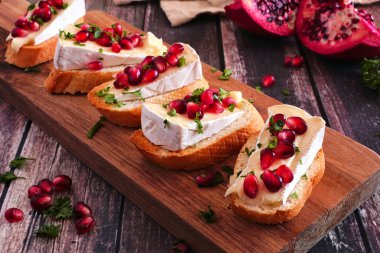 Brie peyniri, nar ve maydanozlu bayram crostini mezeleri. Köy ahşap arka planına karşı servis panosuna yakın dur. Parti yemeği konsepti.
