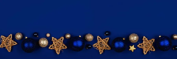 Christmas border banner of dark blue and gold ornaments. Top view on a midnight blue background.