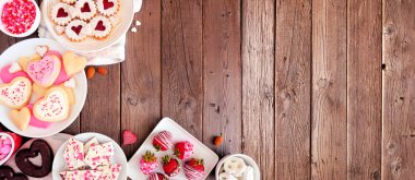 Sevgililer Günü 'nde çeşitli tatlı ve kurabiyelerden oluşan sınır bayrağı. Ahşap arka planda üst manzara. Aşk ve kalp teması. Boşluğu kopyala.