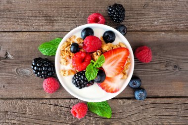 Bir kase yoğurt, sağlıklı taze böğürtlen ve granola. Kırsal bir ahşap arka planda üst görünümü kapat.