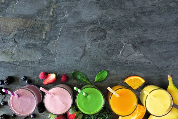 Assorted healthy fruit smoothies. Top view bottom border against a dark background. Copy space.