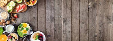 Kenar sınırlı sağlıklı kahvaltı afişi. Meyve, yoğurt, meyve suyu kasesi, besleyici tostlar, mısır gevreği ve yumurta tavası. Kırsal ahşap arka planda üst manzara. Boşluğu kopyala.