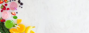 Çeşitli sağlıklı meyve suları. Mermer bir arka planda, tepeden bakan köşe pankartı. Yabanmersini, çilek, yeşil ve turuncu. Boşluğu kopyala.