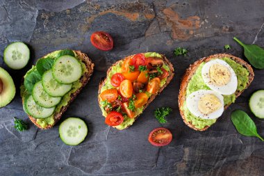 Sağlıklı avokado tostu çeşitleri. Salatalık ıspanak, domates ve yumurta. Koyu renkli bir arkaplan üzerinde üst görünüm.