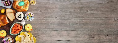 Çeşitli ekmekler, tatlılar ve ikramlar içeren Paskalya masası sahnesi. Ahşap arka planda yan kenarı olan bir pankartın üstünde. Bahar tatili yemekleri..