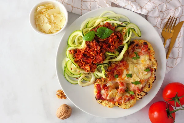 Cauliflower parmesan and zucchini pasta topped with meatless walnut cauliflower bolognese. Above view scene on a marble background. Healthy eating, plant-based meat substitute concept.