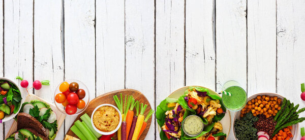 Healthy lunch food bottom border. Table scene with nutritious buddha bowl, lettuce wraps, sandwiches, salad and vegetables. Top view over a white wood background. Copy space.