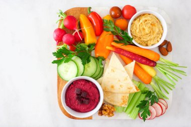 Taze sebze çeşitleri ve bir tabakta humus sosu. Beyaz mermer arka planda üst görünüm.