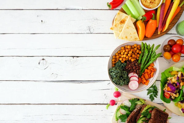 Healthy lunch food side border. Table scene with nutritious hearty bowl, sandwiches, lettuce wraps and vegetables. Above view over a white wood background. Copy space.