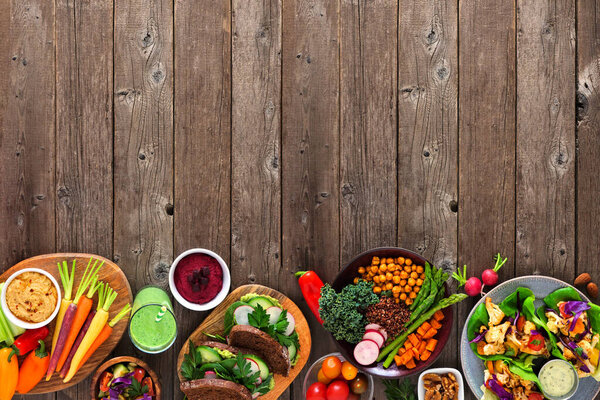 Healthy lunch food bottom border. Table scene with nutritious vegetables, sandwiches, buddha bowl an lettuce wraps. Top view over a dark wood background. Copy space.