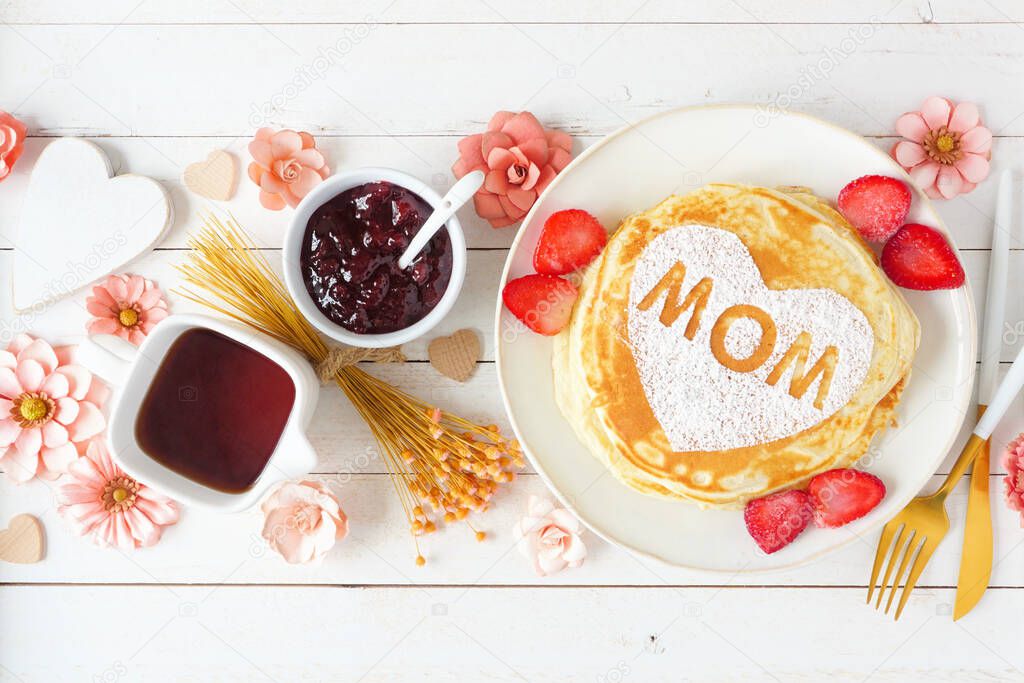 Pancakes with heart shape and MOM letters. Mothers Day breakfast concept. Above view table scene on a white wood background.