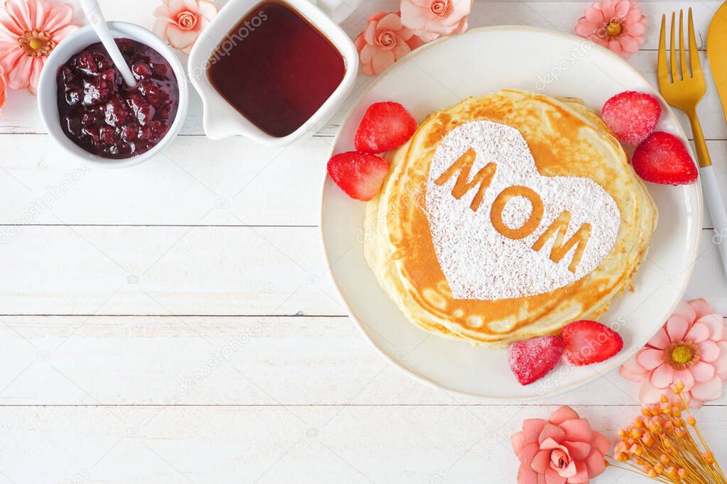 Pancakes with heart shape and MOM letters. Mothers Day breakfast concept. Above view corner border on a white wood background.