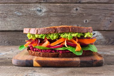 Avokado, pancar humusu, ıspanak turpu ve havuçlu sağlıklı bir süper yiyecek sandviçi. Kırsal ahşap arka planda ahşap bir tahta üzerinde yan görünüm.
