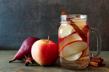 Sonbahar temalı detoks suyu, elmalı, tarçınlı ve kırmızı armut kavanozlu koyu bir arka planda.