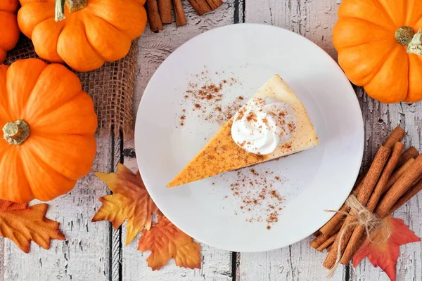 Slice of pumpkin cheesecake with whipped cream, overhead table scene on a white wood background