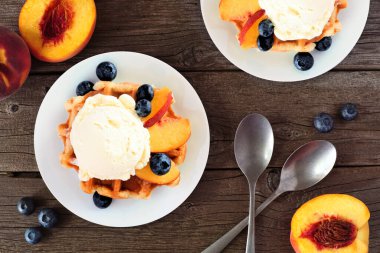 Vanilyalı dondurma, şeftali ve yabanmersinli waffle. Kırsal ahşap arka planlı masa manzarasının üstünde..