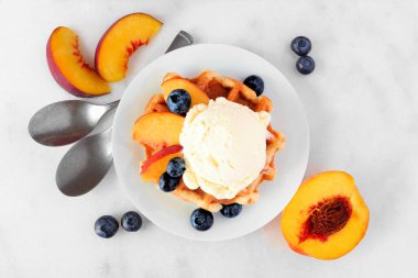 Vanilyalı dondurma, şeftali ve yabanmersinli waffle. Beyaz mermer zemin üzerinde malzeme çerçevesi olan bir tabak. Üst görünüm.