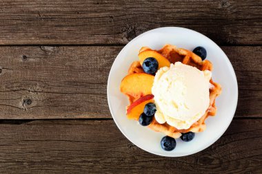 Vanilyalı dondurma, şeftali ve yabanmersinli waffle. Kırsal ahşap arka planda üst görünüm.