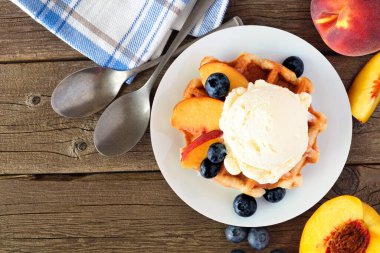 Vanilyalı dondurma, şeftali ve yabanmersinli waffle. Kırsal ahşap arkaplanda en iyi görünüm tablosu.