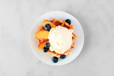 Vanilyalı dondurma, şeftali ve yabanmersinli waffle. Beyaz mermer arka planda üst görünüm.