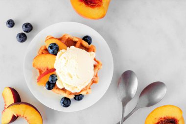 Vanilyalı dondurma, şeftali ve yabanmersinli waffle. Beyaz mermer arkaplanlı yukarıdaki tablo sahnesi.