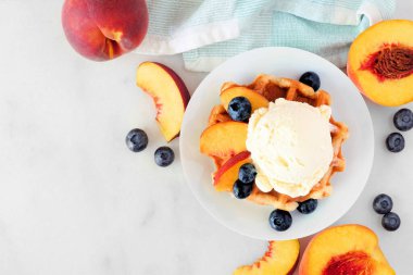 Vanilyalı dondurma, şeftali ve yabanmersinli waffle. Beyaz mermer zemin ile üst görünüm tablo sahnesi.