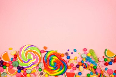 Renkli tatlı şekerler. Pembe arka planda alt görünüm sınırının üstünde.