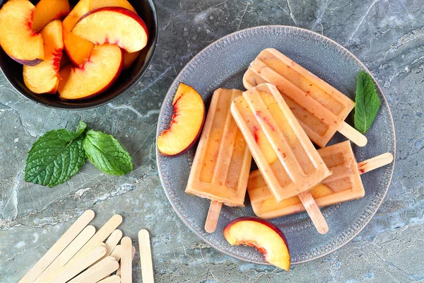 Healthy peach yogurt ice pops on a plate, top view table scene against a dark stone background