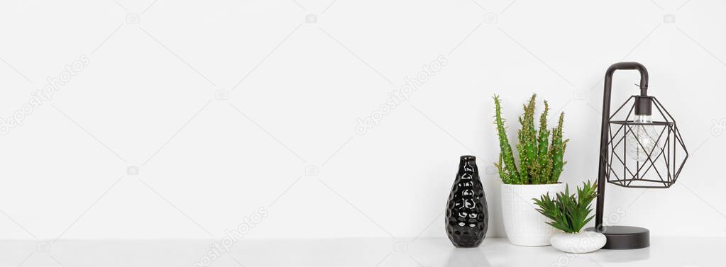 Home decor on a shelf. Industrial style lamp, vase and plants. White shelf and wall. Banner with copy space.