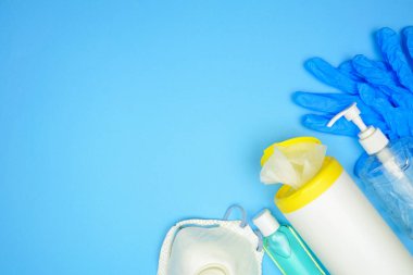 Coronavirus önleme ekipmanı, n95 maskesi, el dezenfektanı, temizleyici mendil, eldiven. Üstteki görünüm kenarı mavi arkaplan üzerinde kopyalama alanı ile.