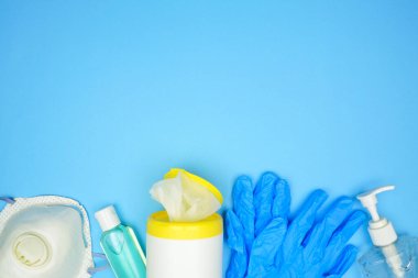 COVID 19 önleme ekipmanı, n95 maske, el dezenfektanı, temizleme bezi, eldiven. Kopya alanı olan mavi bir arkaplan üzerindeki görünüm sınırının üzerinde.