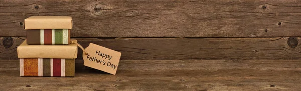 Happy Father\'s Day gift tag and two stacked boxes. Side view banner against a rustic brown wood background.