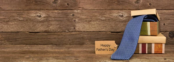 Happy Father\'s Day gift tag and two stacked boxes with necktie gift. Side view banner against a rustic brown wood background.