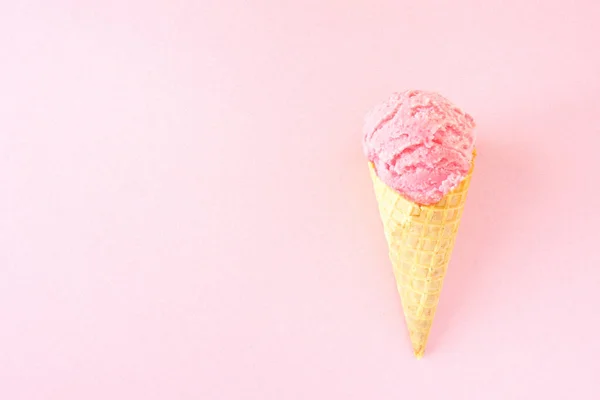 Single ice cream cone with strawberry ice cream over a pink background. Top view with copy space.
