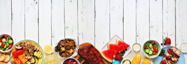 Yaz barbeküsü ya da piknik yemekleri. Çeşitli ızgara etler, sebzeler, meyveler, salata ve patates. Beyaz ahşap bir arka plan üzerinde üst görünüm. Boşluğu kopyala.