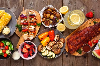 Yaz barbeküsü ya da piknik masası sahnesi. Izgara et, sebze, meyve, salata ve patates. Koyu bir ahşap arkaplan üzerinden yukarıdan aşağı görünüm.