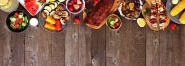 Yaz barbeküsü ya da piknik yemekleri kırsal bir tahta afişin üst sınırında. Çeşitli ızgara etler, sebzeler, meyveler, salata ve patates. Kopyalama alanı ile görünümün üstünde.