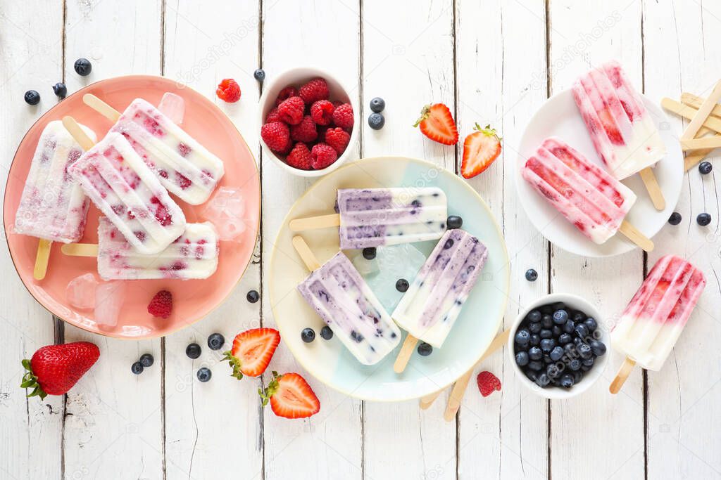Variety of homemade berry yogurt popsicles. Top view table scene on a rustic white wood background.